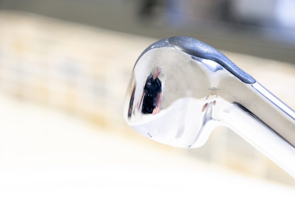 Detail of a curved chrome tap spout above a pale kitchen benchtop
