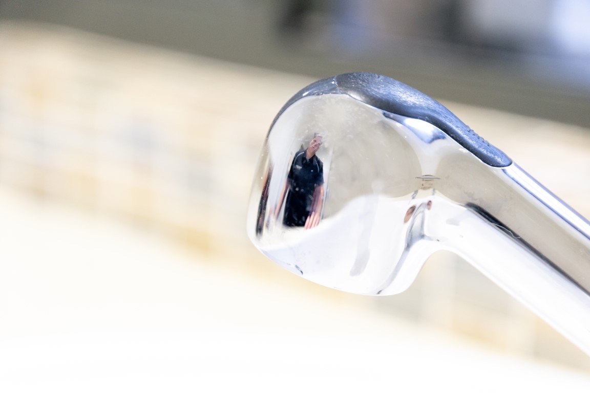 Chrome tap spout reflecting a plumber in a dark work shirt