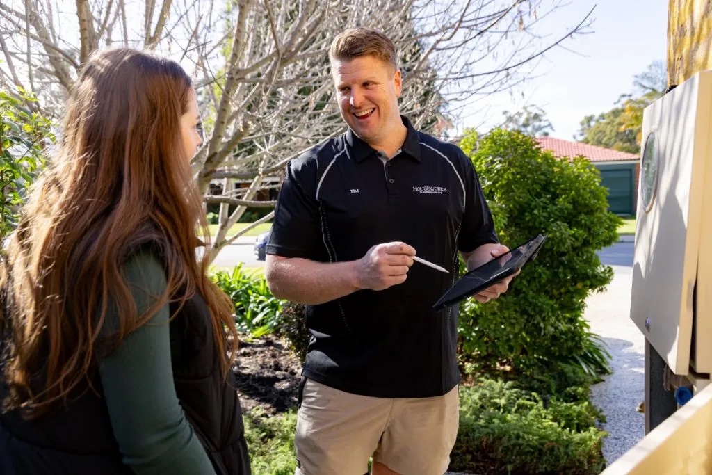 HouseWorks plumber holding a tablet and stylus while talking with a customer outdoors